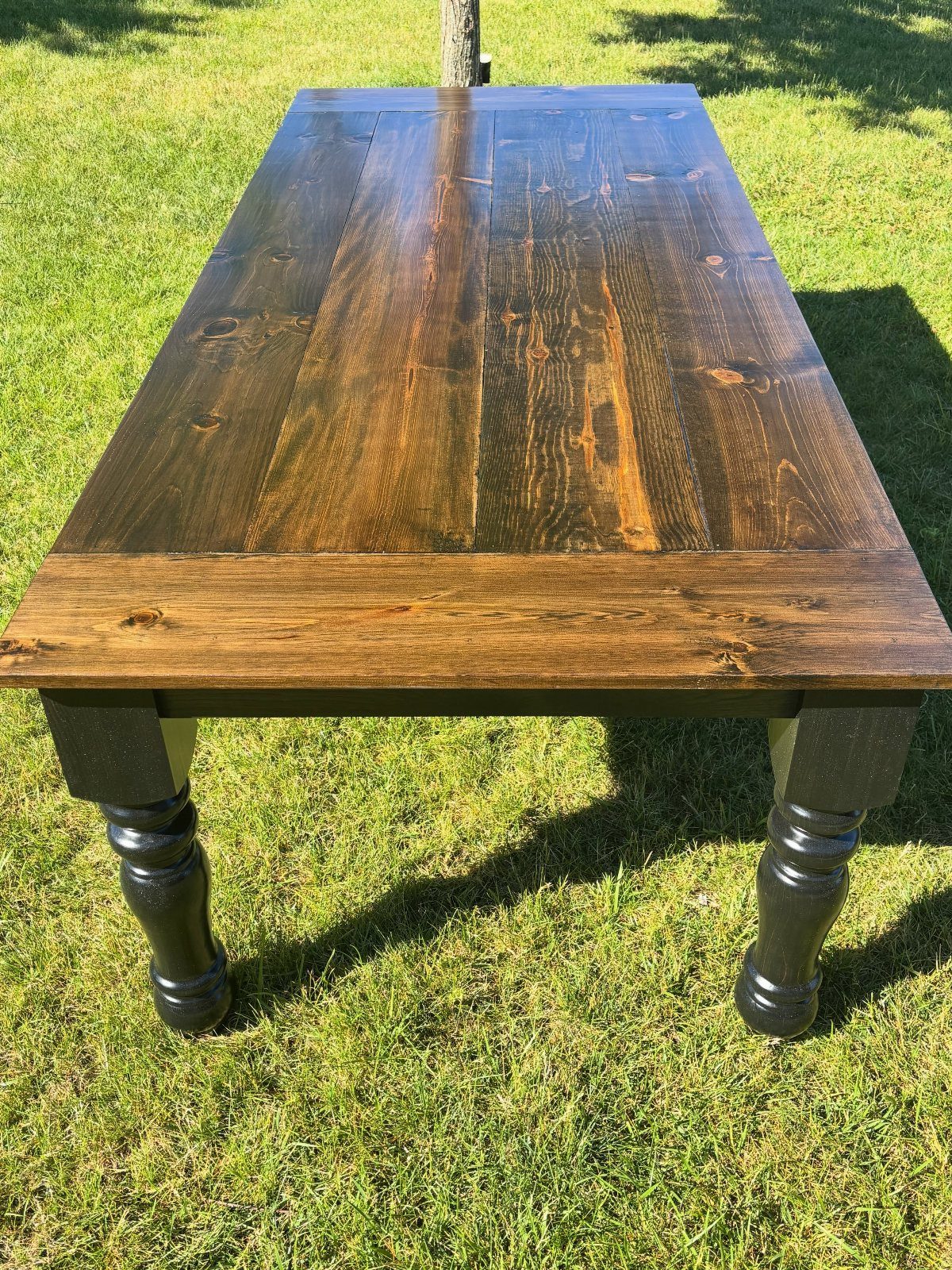 Dark walnut dining table with turned black legs standing on a green lawn.