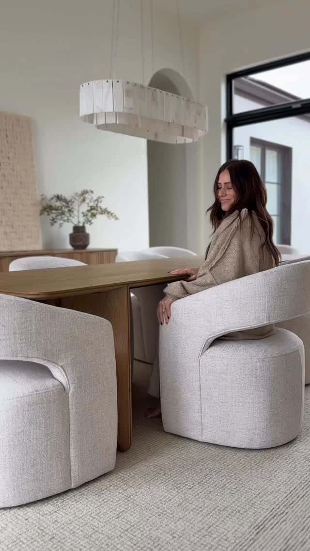 Walnut dining table with large, curved cream upholstered chairs in a modern room.