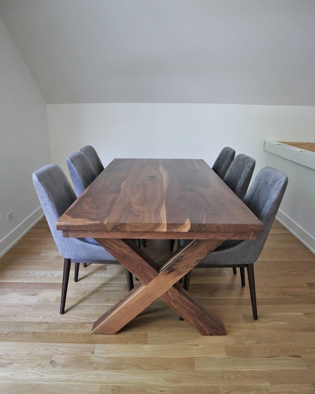 Walnut dining table with X-base and grey upholstered chairs on light wood flooring.